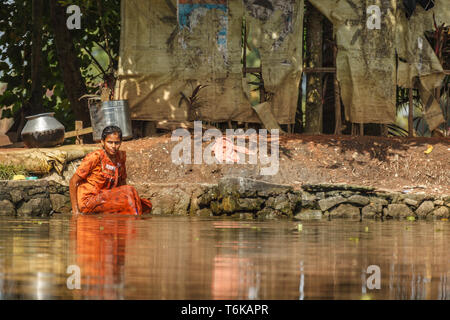 Libre de jeune femme dans un sari orange assis dans la rivière devant une tente maison sur pilotis en Inde Banque D'Images