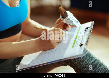 Gros plan sur jeune femme en vêtements de remise en forme avec des protéines brutes de remplissage de la barre de chocolat repas dans la maison moderne. Banque D'Images