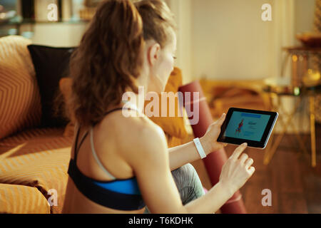 Vus de derrière, jeune femme en vêtements de sport moderne à l'aide d'entraîneur personnel de conditionnement physique app en PC tablette. Banque D'Images