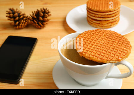 L'un placé sur Stroopwafel la tasse de café chaud et une assiette de sa pile en arrière-plan avec un cellulaire et des cônes de pin sec Banque D'Images