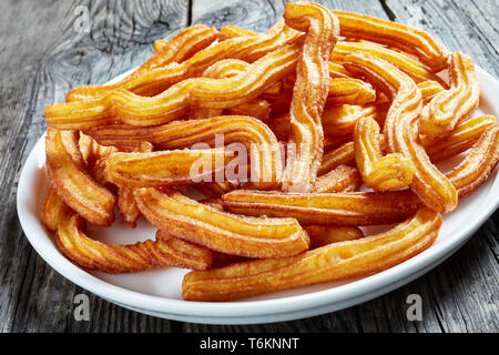 Churros frits délicieux servi sur une plaque blanche sur une table en bois, close-up Banque D'Images