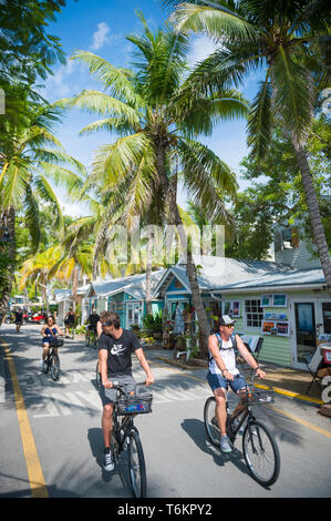 KEY WEST, Floride, USA - Septembre 2018 : Visiteurs aller en vélo le long d'un vide rue de la vieille ville bordée de maisons aux couleurs vives convertis en magasins. Banque D'Images