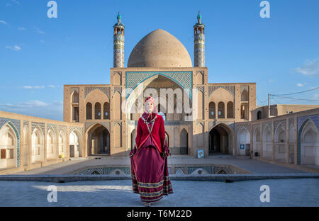 Belle jeune femme iranienne habillés en costume traditionnel rouge dans une mosquée à Kashan Banque D'Images