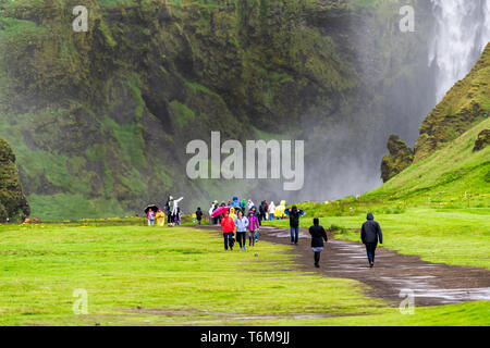 Skogafoss, Islande - 14 juin 2018 : Cascade sur falaise avec green grass meadow et beaucoup de touristes avec des gens qui marchent sur le sentier des ponchos de pluie route mo Banque D'Images