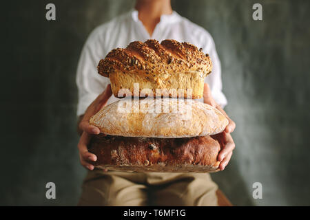 Close up of female chef holding différents types de pain dans la main. Baker montrant différents types de pain pain contre fond gris. Banque D'Images
