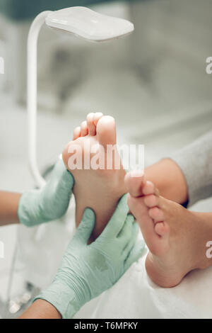 Maître concentré dans des gants en caoutchouc vert avec massage des jambes traitement de durcissement Banque D'Images