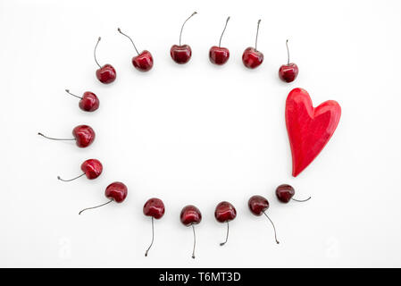 Cadre rond de cerises mûres et de bois, coeur rouge sur fond blanc. Banque D'Images