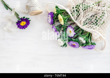 Bouquet d'asters colorés dans un sac-filet et ruban décoratif, sur fond de bois blanc. Banque D'Images