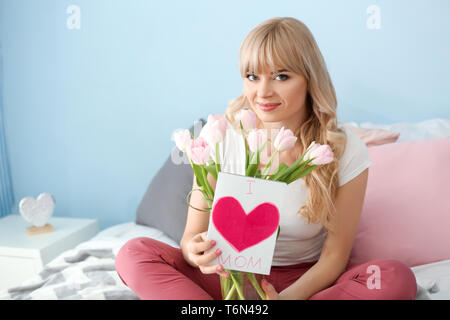 Portrait de jeune femme avec bouquet de tulipes à la main et carte dans une chambre. Célébration de la fête des Mères Banque D'Images