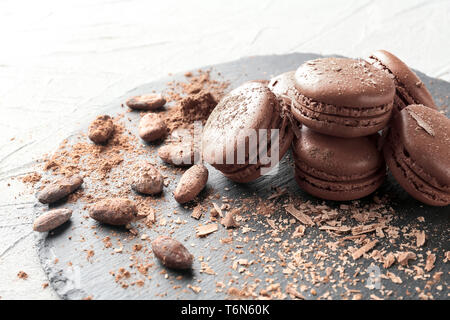 Plaque en ardoise avec de délicieux macarons au chocolat et grains de cacao sur la table Banque D'Images