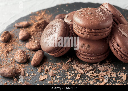 Plaque en ardoise avec de délicieux macarons au chocolat et cacao en fèves, gros plan Banque D'Images