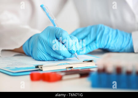 Travailleur de laboratoire sous forme de remplissage près de tubes à essai avec des échantillons de sang sur la table Banque D'Images