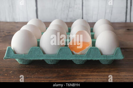 Les œufs blancs sur des conteneurs en carton cyan, avec un oeuf cassé en deux Banque D'Images