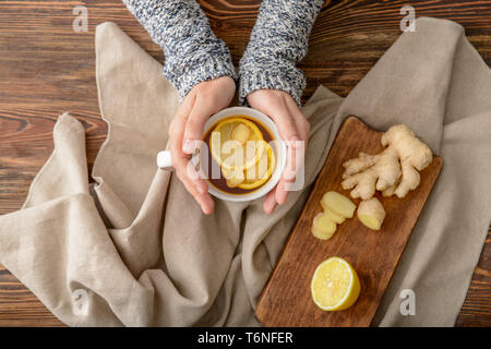 Femme tenant une tasse de thé au citron et gingembre sur table en bois Banque D'Images