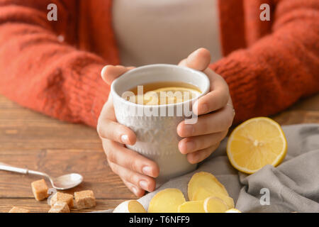 Femme tenant une tasse de thé au citron et gingembre sur table en bois Banque D'Images