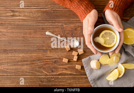 Femme tenant une tasse de thé au citron et gingembre sur table en bois Banque D'Images