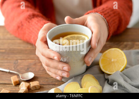 Femme tenant une tasse de thé au citron et gingembre sur table en bois Banque D'Images
