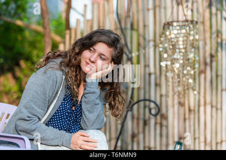 Jeune femme face à la route happy smiling en bambou zen garden avec décorations brillant Wind Chimes sitting on chair Banque D'Images