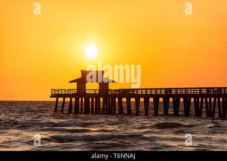Naples, Florida sunset orange jaune libre dans le golfe du Mexique avec sun et Pier jetée en bois d'ossature à l'horizon et les vagues de l'océan Banque D'Images