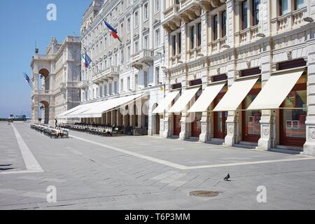 Façade de maison avec des auvents et des rangées de chaises vides devant un café sur la Piazza Unita d'Italia, Trieste, Italie Banque D'Images