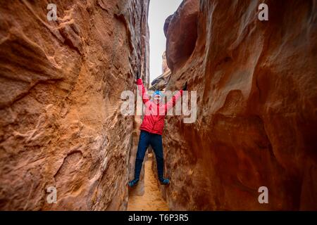 Jeune femme debout dans l'écart entre les roches, Sand Dune Arch, Arches National Park, près de Moab, Utah, USA Banque D'Images