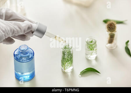 Des gouttes d'échantillon dans femme avec bouteille sur des plantes en laboratoire de table Banque D'Images