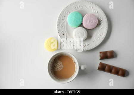 Plaque avec de délicieux macarons colorés et tasse de café sur fond blanc Banque D'Images