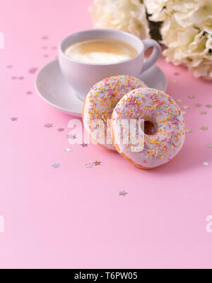 Tasse de cappuccino chaud et deux beignets de fleurs sur fond rose. Banque D'Images