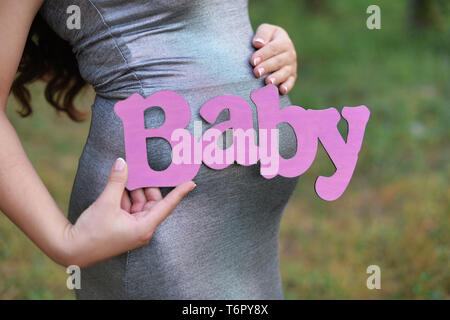 Fille enceinte avec le ventre avec des lettres d'attente inscription lettre rose dans ses mains dans un parc en plein air Banque D'Images