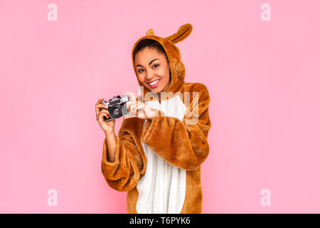 Jeune femme en bunny permanent kigurumi isolé sur fond rose holdign caméra film joyeux sourire prendre des photos Banque D'Images