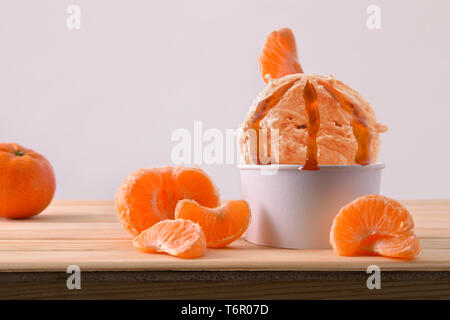 La crème glacée Mandarin tasse décorée avec des segments de mandarines sur une table en bois. Composition horizontale. Vue de face. Banque D'Images