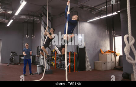 Les jeunes hommes sportifs escalade sur corde en salle de sport Banque D'Images