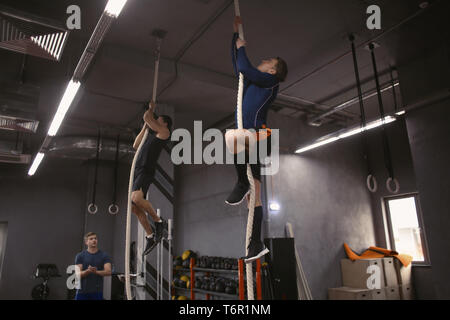 Les jeunes hommes sportifs escalade sur corde en salle de sport Banque D'Images