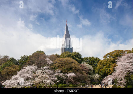 Jardin National de Shinjuku Gyoen avec Fleur de cerisier, le NTT Docomo Yoyogi Building en arrière-plan et bleu, ciel nuageux Banque D'Images