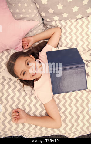 Lit enfant fille lay read book vue d'en haut. Kid se préparer à aller au lit. Temps agréable dans une chambre confortable. Kid fille cheveux longs pyjamas mignons vous détendre et lire livre. Encourager les habitudes utiles. Satisfait de professionnels. Banque D'Images