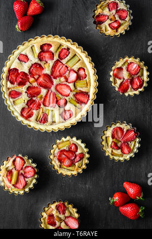 Des tartelettes aux fraises et rhubarbe sur fond de bois noir. Vue d'en haut. Style rustique Banque D'Images