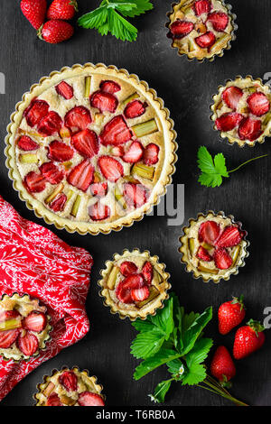 Des tartelettes aux fraises et rhubarbe sur fond de bois noir. Vue d'en haut. Style rustique Banque D'Images