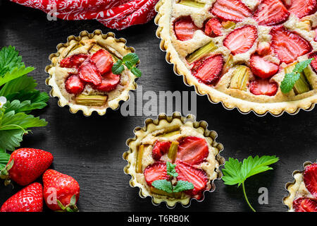 Des tartelettes aux fraises et rhubarbe sur fond de bois noir. Vue d'en haut. Style rustique Banque D'Images