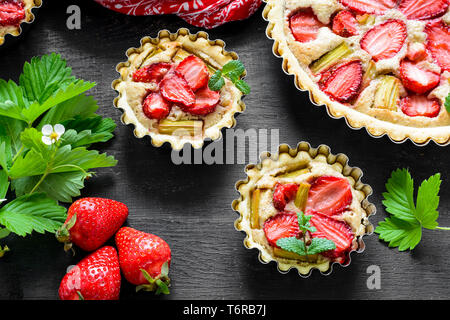 Des tartelettes aux fraises et rhubarbe sur fond de bois noir. Vue d'en haut. Style rustique Banque D'Images