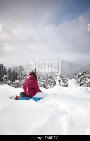 Jeune femme assise sur le flanc de montagne et se réjouit à la vue sur l'horizon en face de magnifiques pins en hiver. Billet d'arrière-plan avec sno Banque D'Images