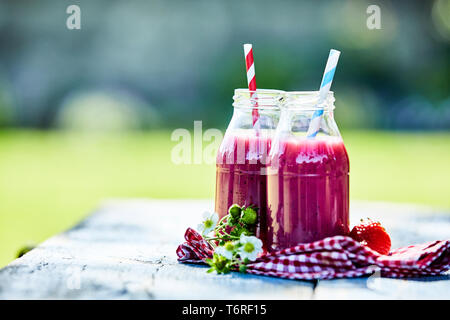 Lumineux aux couleurs éclatantes des smoothies fraises dans des bocaux en verre sur une table de pique-nique d'été en plein air. Banque D'Images