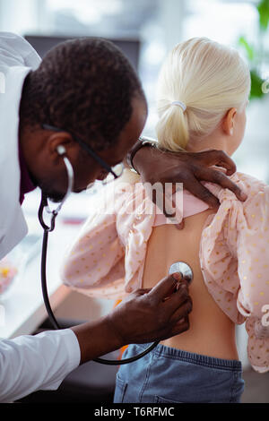 Médecin à l'aide de stéthoscope pendant l'écoute de poumons de jeune fille blonde Banque D'Images