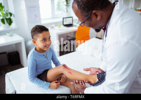 Cute boy venant de pédiatre après avoir gratté la jambe Banque D'Images