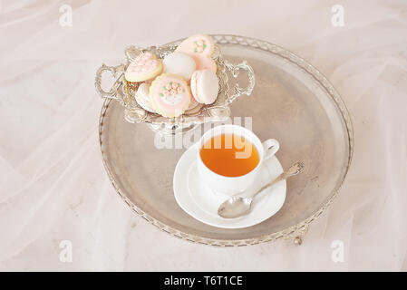 Plateau d'argent avec une tasse de thé et des macarons sur un tableau blanc en bois dans une pièce blanche. Banque D'Images
