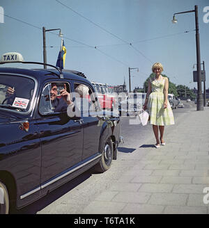 Chauffeur de taxi dans les années 60. Un chauffeur de taxi se présente comme s'il essaie de dire quelque chose d'intéressant à l'sur le siège arrière. Il est cependant plus intéressé à examiner la blonde jeune fille sur le trottoir. La Suède 1960 ref BV71-5 Banque D'Images