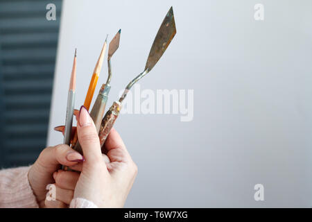 Libre de womans hand holding tools pour la peinture à l'huile, les pinceaux et la spatule, contre une toile blanche, selective focus Banque D'Images