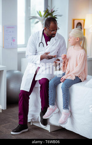 Fille blonde portait un jean et un chemisier rose assis près de médecin Banque D'Images