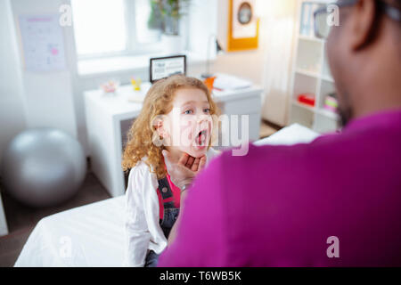 Girl opening bouche montrant sa gorge tandis que médecin de passage Banque D'Images