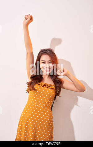 Belle jeune femme gaie en orange portant robe à pois danse et posant sur mur beige. Bonne humeur. Haut les mains ! Les émotions des gens beauté Fash Banque D'Images