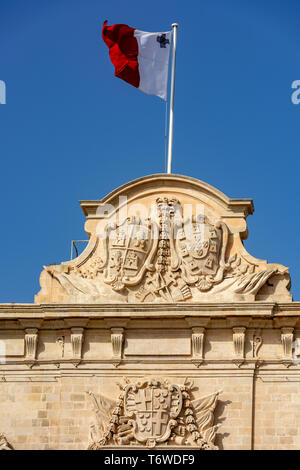 Le drapeau maltais survole les armoiries de Castille et de León, et du Portugal qui décorent la pièce maîtresse de l'Auberge baroque de Castille. Banque D'Images